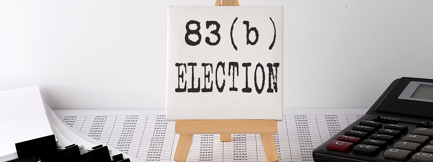 Easel with painting for words "83(b) election," with a calculator and a spreadsheet