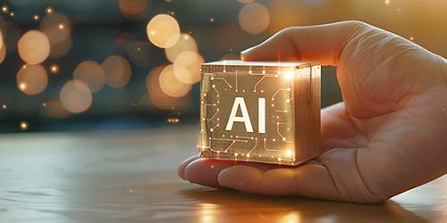 Image of a hand holding a block with the letters "AI" imprinted on it and lines that are reminiscent of computer circuitry